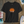 Black t-shirt with a sun graphic and text on a wooden surface