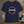 Navy blue t-shirt with 'PLUTO' graphic on a wooden surface with space-themed items.